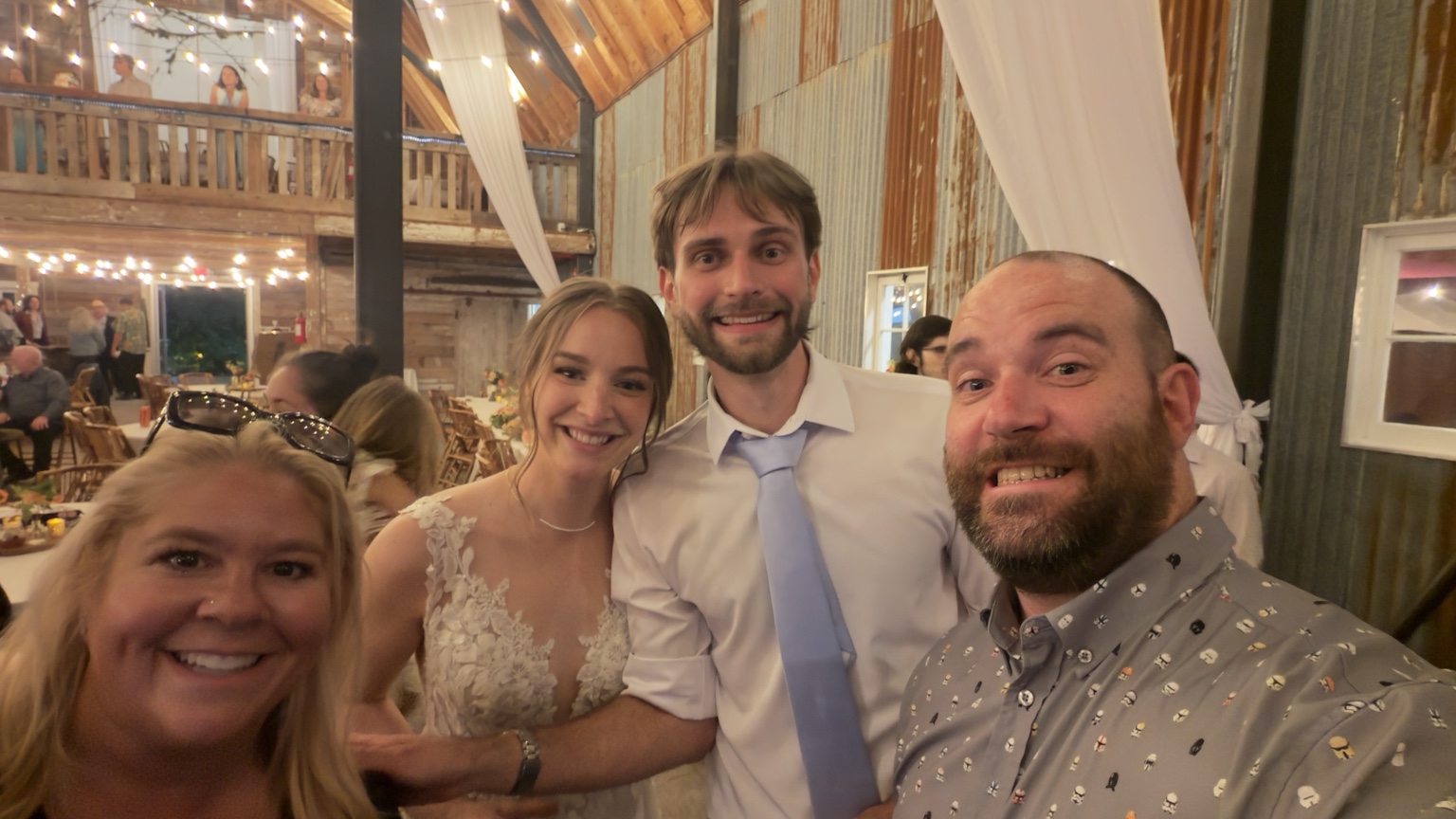 Wedding group posing beneath the barn’s warm string lights