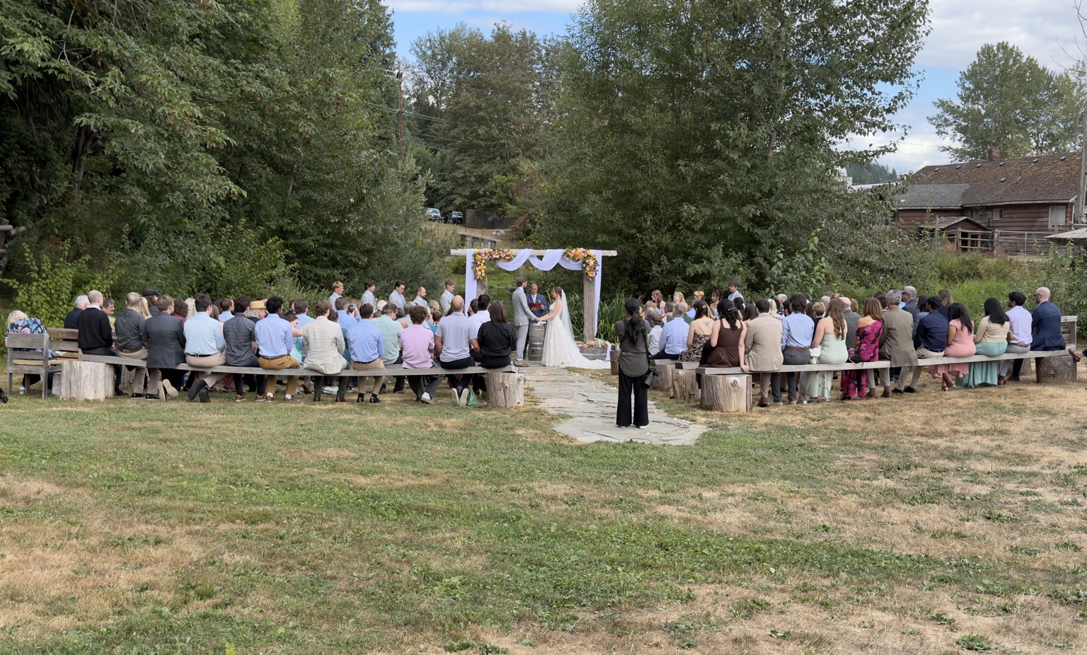 Outdoor wedding ceremony with guests seated around a floral arch