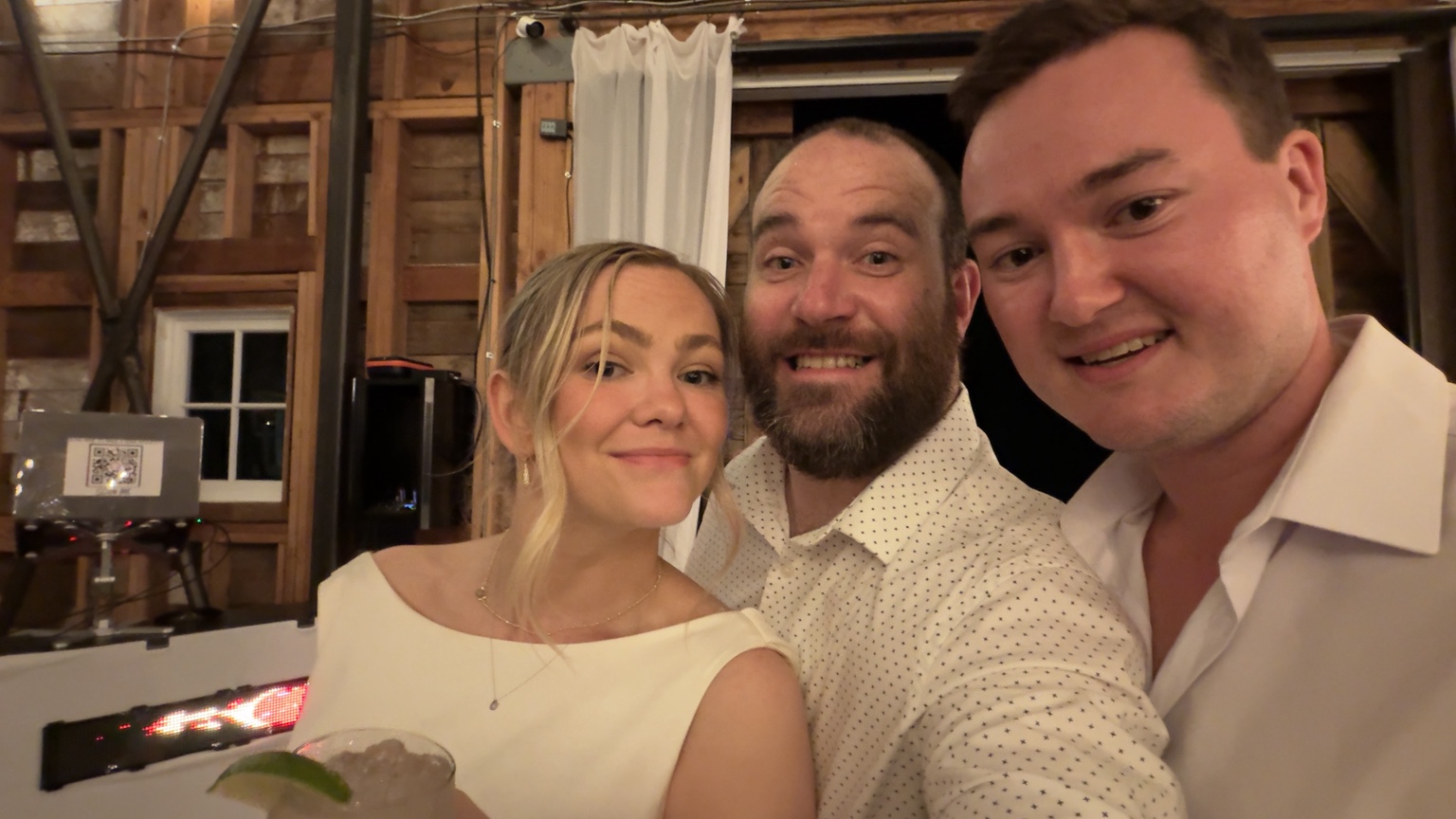Three smiling people posing together beside the wedding DJ booth